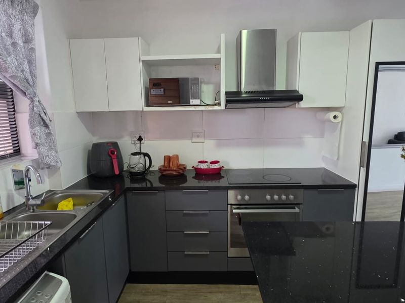 A modern kitchen featuring dark grey lower cabinetry, white upper cabinets, black granite countertops, and integrated stainless steel appliances.
