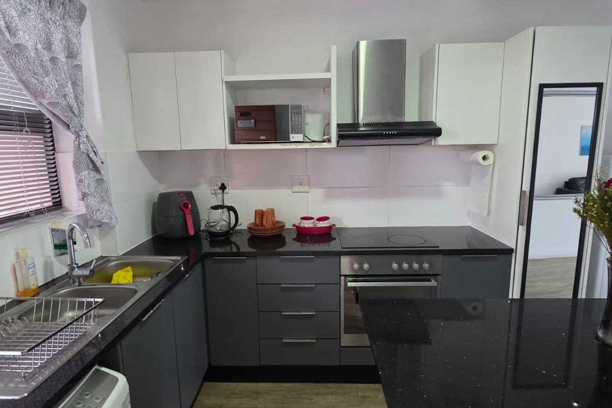 A modern kitchen featuring dark grey lower cabinetry, white upper cabinets, black granite countertops, and integrated stainless steel appliances.