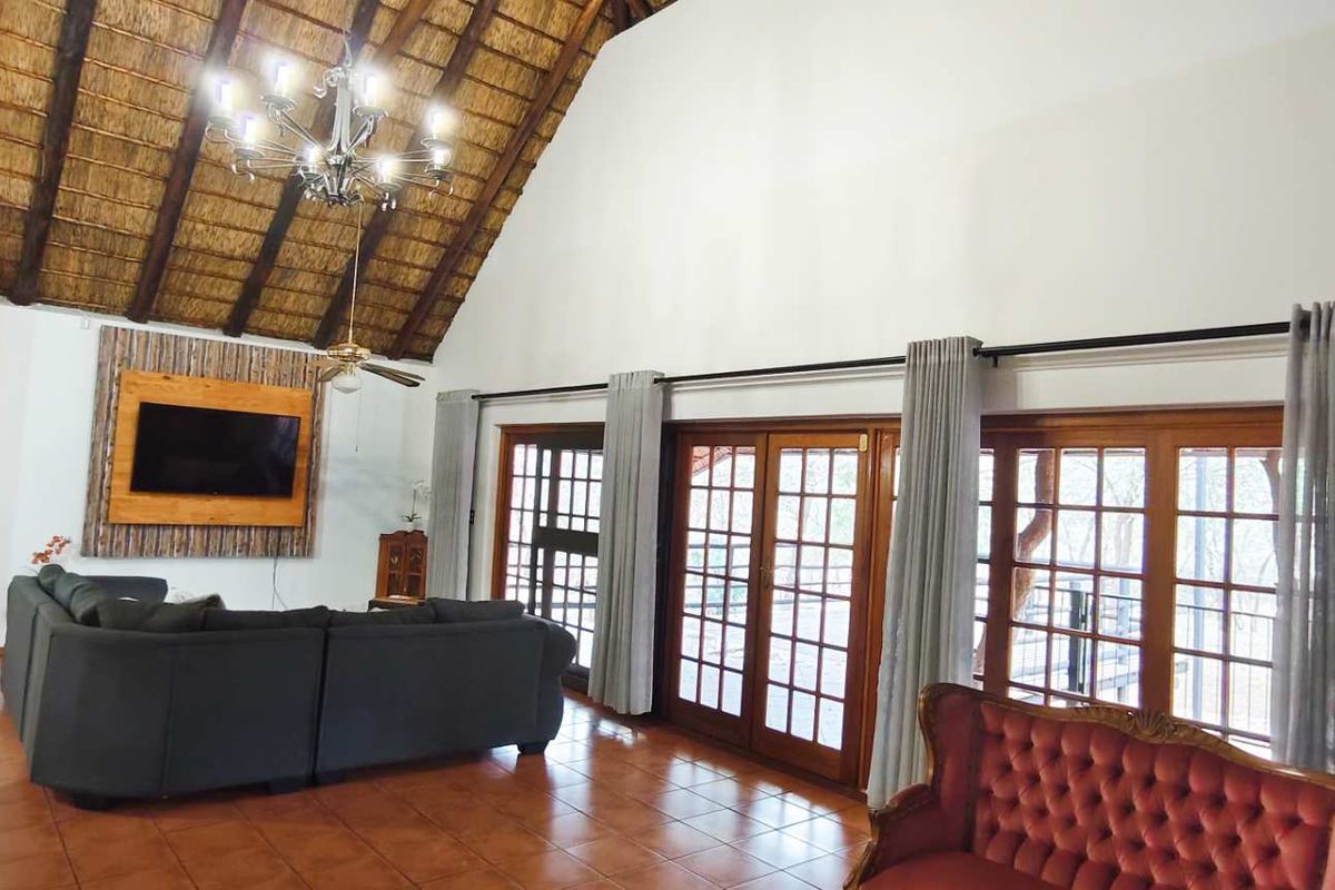 Spacious living area featuring a high vaulted thatched ceiling, terracotta floor tiles, and large wooden French doors opening to the exterior.