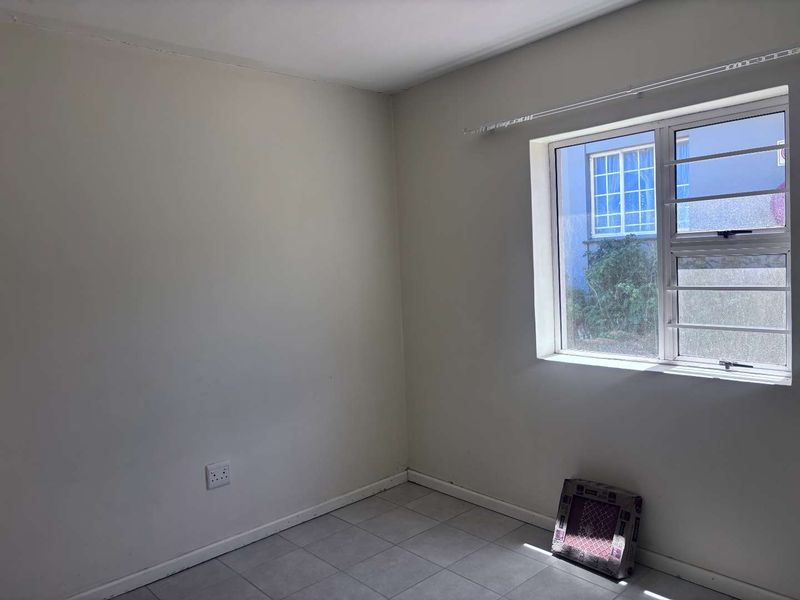 An empty bedroom featuring tiled flooring, a window with security bars, and neutral wall finishes, offering a blank canvas for personalization.