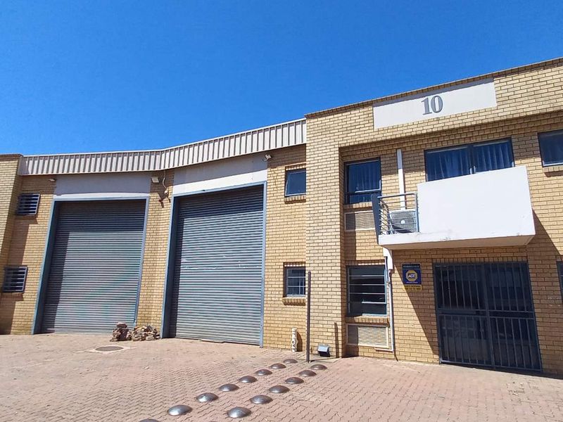 Front elevation of an industrial warehouse complex featuring brick facade, multiple roller shutter doors, and paved access area.