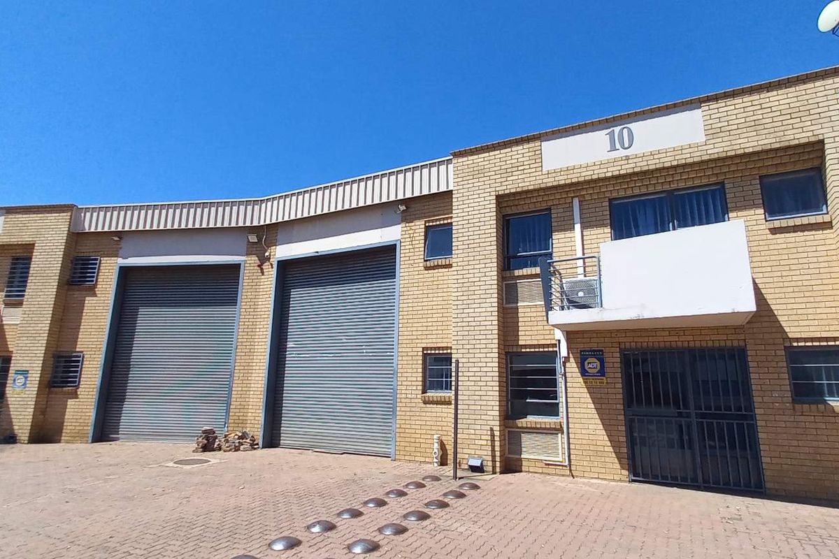 Front elevation of an industrial warehouse complex featuring brick facade, multiple roller shutter doors, and paved access area.