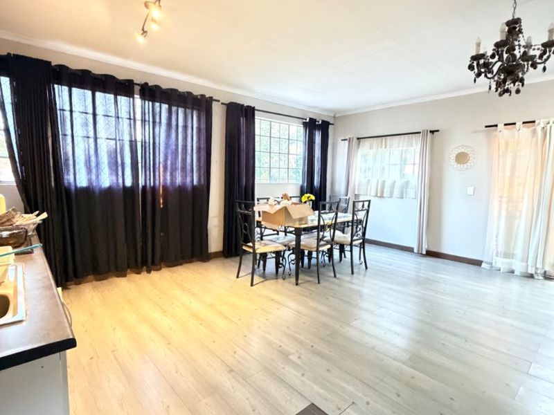 Spacious open-plan living and dining area featuring light-toned laminate flooring, a mix of tiled flooring, and classic lighting fixtures.