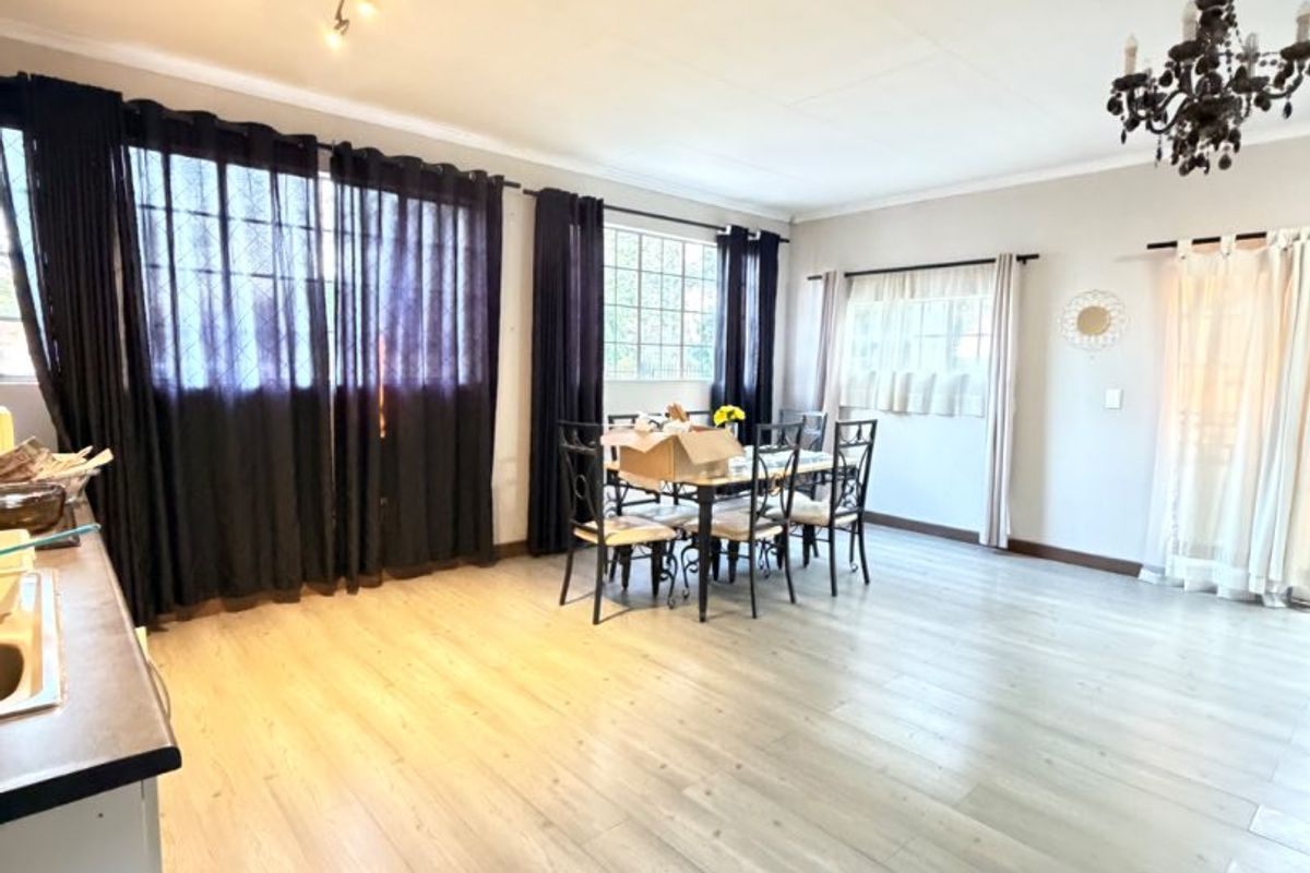 Spacious open-plan living and dining area featuring light-toned laminate flooring, a mix of tiled flooring, and classic lighting fixtures.