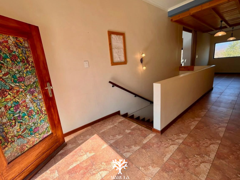 Spacious hallway featuring decorative stained glass door, terracotta-style tiled flooring, and a staircase with a solid balustrade leading to the upper level.