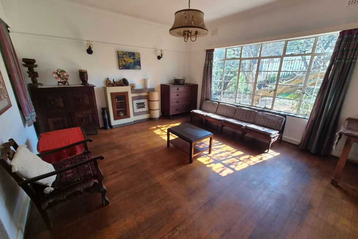 A spacious living room featuring original hardwood flooring, large steel-framed windows providing natural light, and a classic picture rail detail.