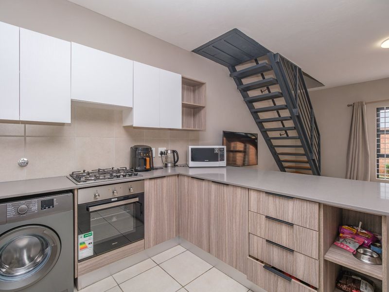 Modern open-plan kitchen featuring stone countertops, built-in oven, gas hob, and integrated laundry space, complemented by a contemporary metal staircase.