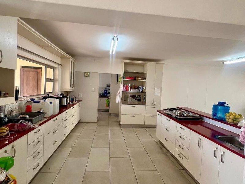 Spacious kitchen featuring extensive white cabinetry, red laminate countertops, built-in oven, and large format floor tiles with a functional galley layout.