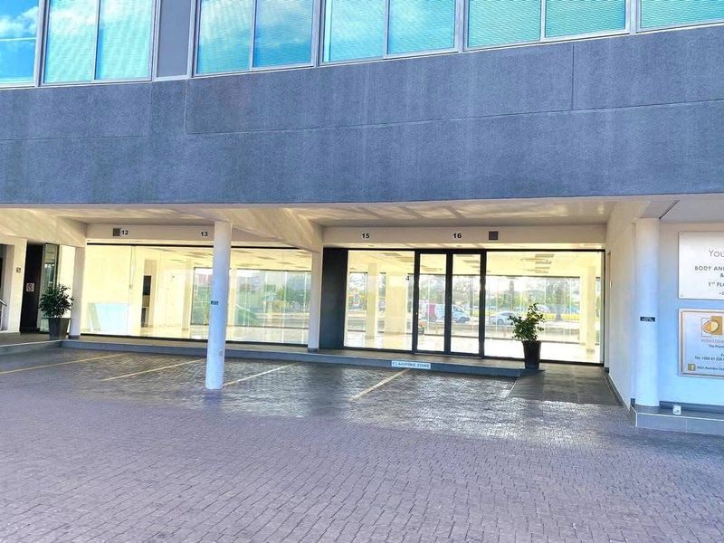 Front exterior view of a commercial retail property featuring a paved driveway, covered parking bays, and large glass storefront windows.