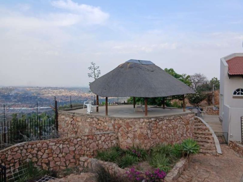 Rear exterior view featuring a circular thatched gazebo, stone retaining walls, and a paved pathway overlooking the surrounding landscape.