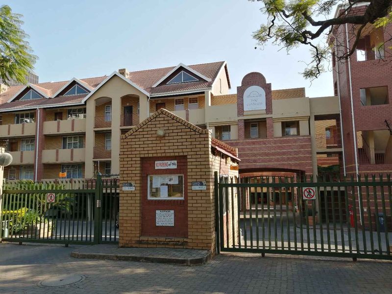 Front exterior view of The Gables apartment complex, featuring a brick facade, tiled roofing, secure gated entrance, and a brick guard house.