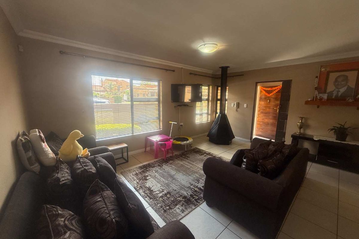 A living room featuring tiled flooring, a freestanding fireplace, and natural light through large windows with venetian blinds.