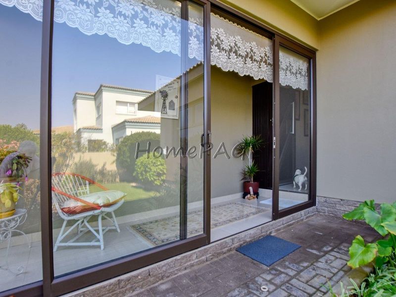 A covered patio area featuring large sliding glass doors, tiled flooring, and direct access to the outdoor garden space.