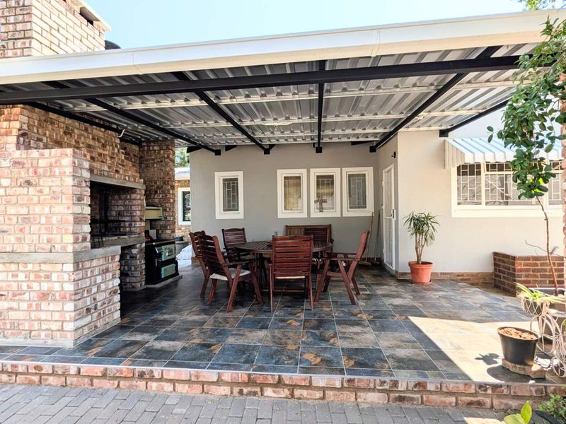 Covered outdoor patio featuring a built-in brick braai, tiled flooring, and a sturdy corrugated metal roof structure, ideal for outdoor entertaining.