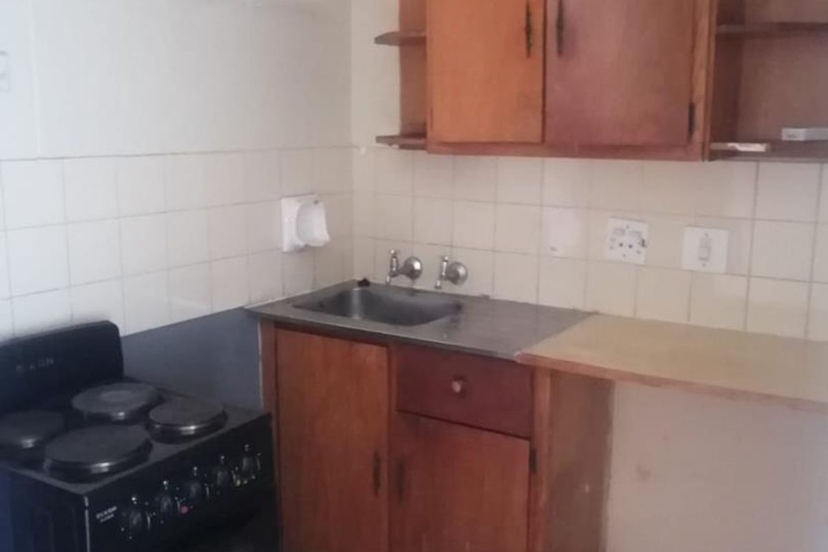 A compact kitchen featuring dated wooden cabinetry, a stainless steel sink, ceramic tiling, and a freestanding electric stove.