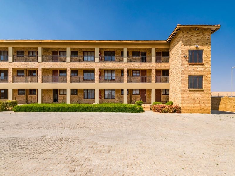 A well-maintained multi-story apartment building featuring a face brick facade, paved driveway, and private balconies with metal railings.