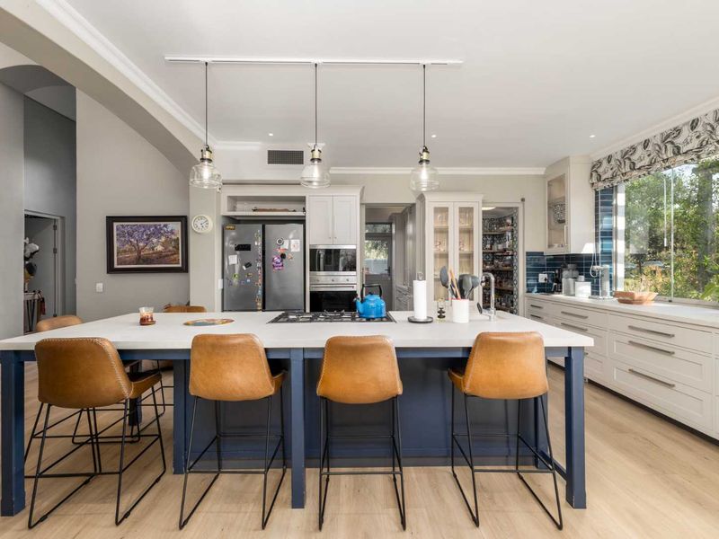 Modern kitchen featuring a large central island with gas cooktop, ample built-in cabinetry, tiled backsplash, and integrated appliances, flowing into a walk-in pantry area.