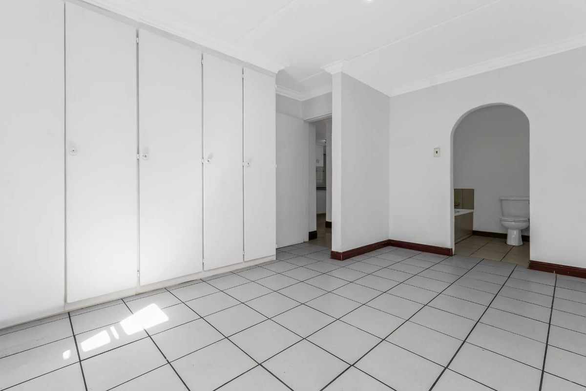 An empty bedroom featuring built-in cupboards, tiled flooring, and an arched doorway leading to an en-suite bathroom.