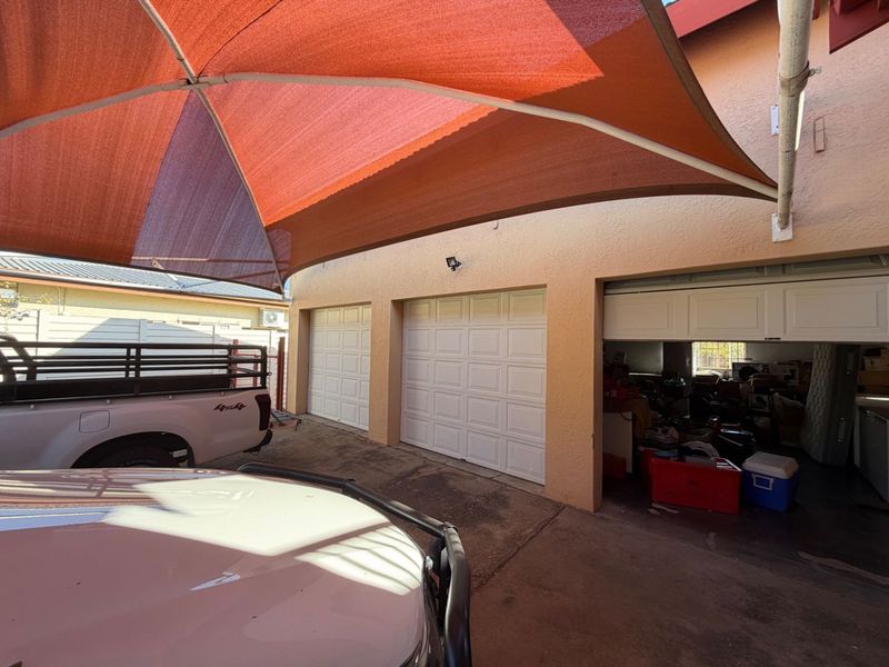 A triple garage featuring white sectional doors, a large overhead shade sail, and a concrete driveway area.