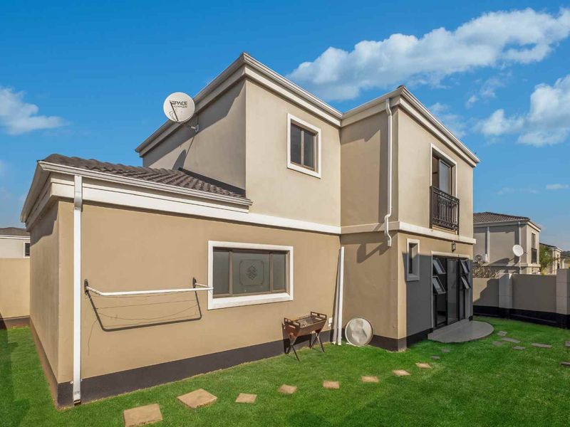 Rear view of the property featuring a landscaped lawn, stone pathway, sliding door access, and a balcony with metal railing.