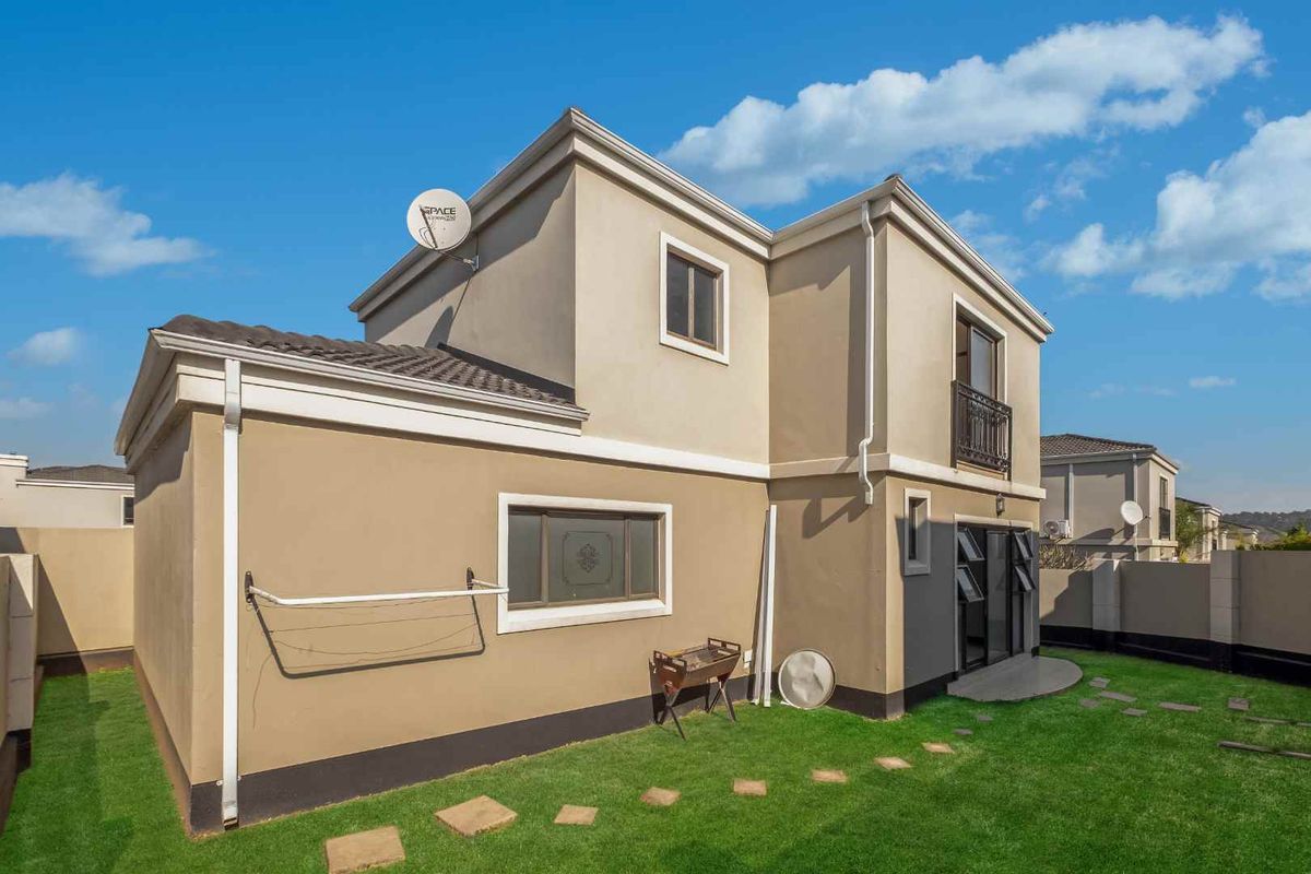 Rear view of the property featuring a landscaped lawn, stone pathway, sliding door access, and a balcony with metal railing.