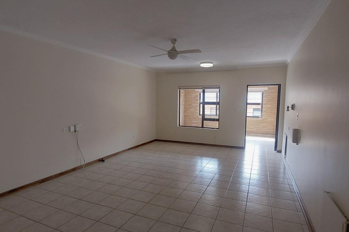 Spacious, empty living area featuring neutral tiled flooring, a ceiling fan, and natural light through aluminium-framed windows leading to an outdoor space.