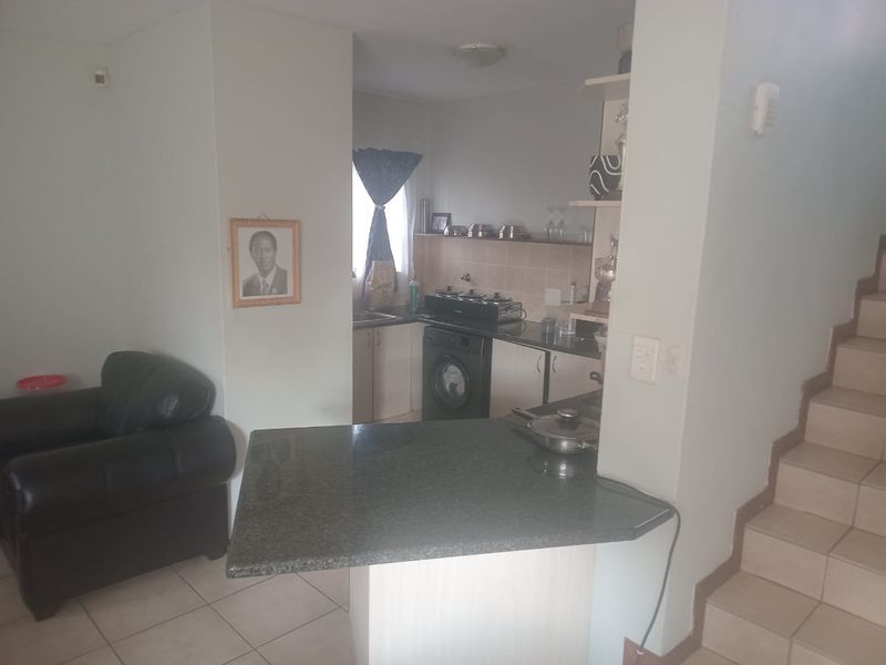 Open plan kitchen area featuring a granite breakfast bar, built-in cabinetry, and tiled flooring, adjacent to the staircase.