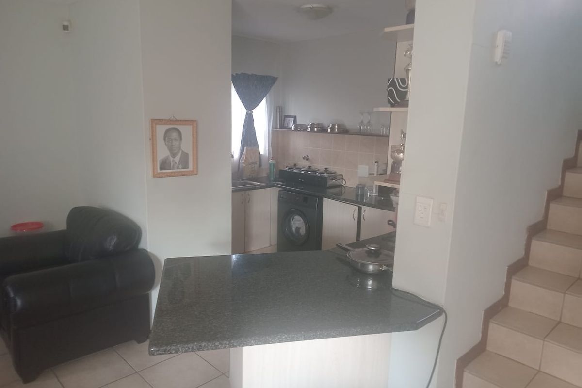 Open plan kitchen area featuring a granite breakfast bar, built-in cabinetry, and tiled flooring, adjacent to the staircase.