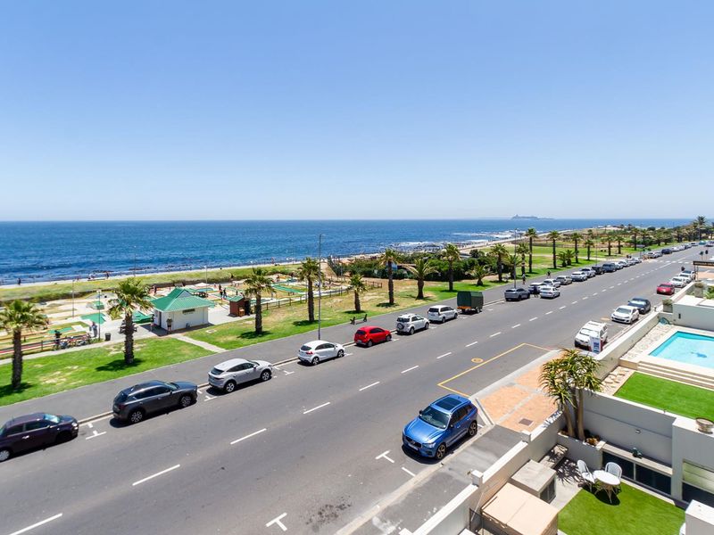 Elevated coastal view overlooking the ocean, public park, and street, featuring a private swimming pool and landscaped lawn area in the foreground.