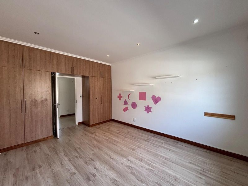 A spacious bedroom featuring wood-look laminate flooring, extensive built-in cabinetry, and recessed ceiling lighting, presenting a clean and functional space ready for personalization.