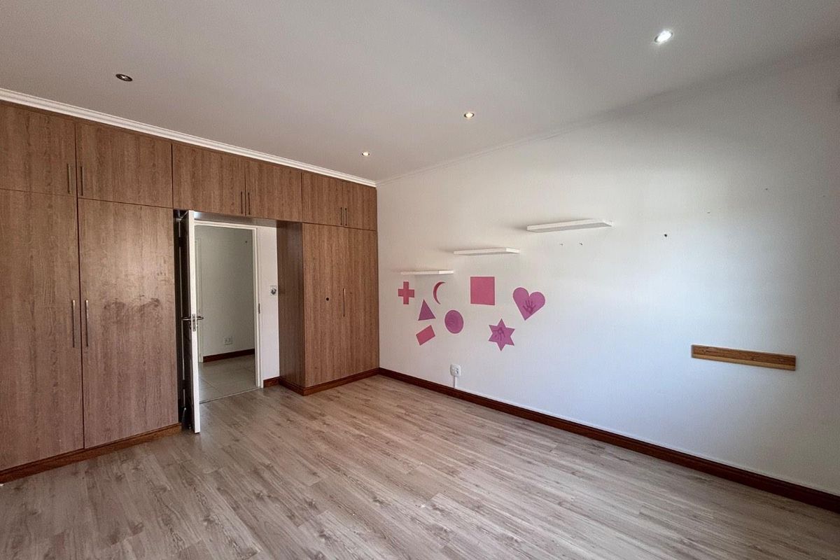 A spacious bedroom featuring wood-look laminate flooring, extensive built-in cabinetry, and recessed ceiling lighting, presenting a clean and functional space ready for personalization.