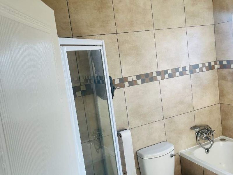 A functional bathroom featuring a shower enclosure, bathtub, and toilet with neutral-toned wall and floor tiling.