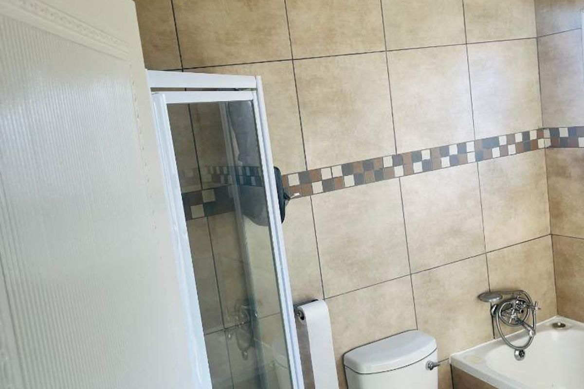 A functional bathroom featuring a shower enclosure, bathtub, and toilet with neutral-toned wall and floor tiling.
