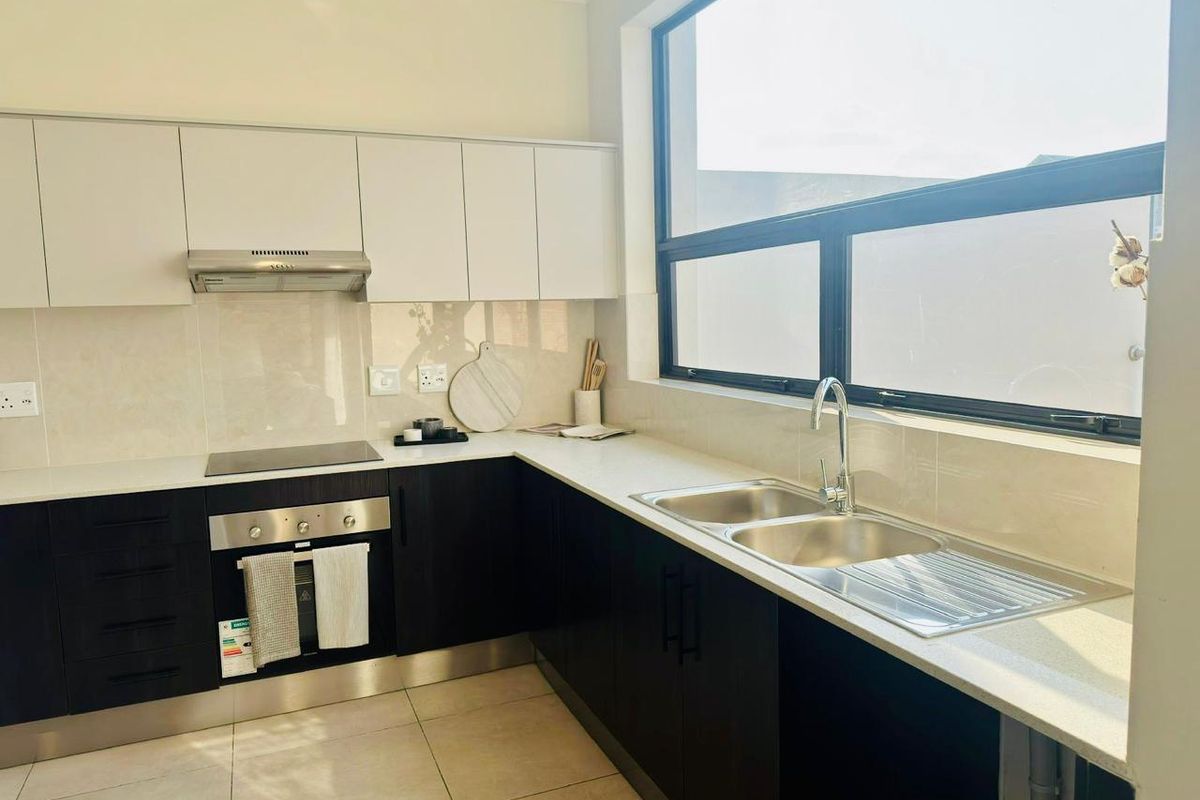 Modern kitchen featuring dark lower cabinetry, white upper cabinets, stone countertops, a built-in oven, hob, extractor fan, and a double stainless steel sink.