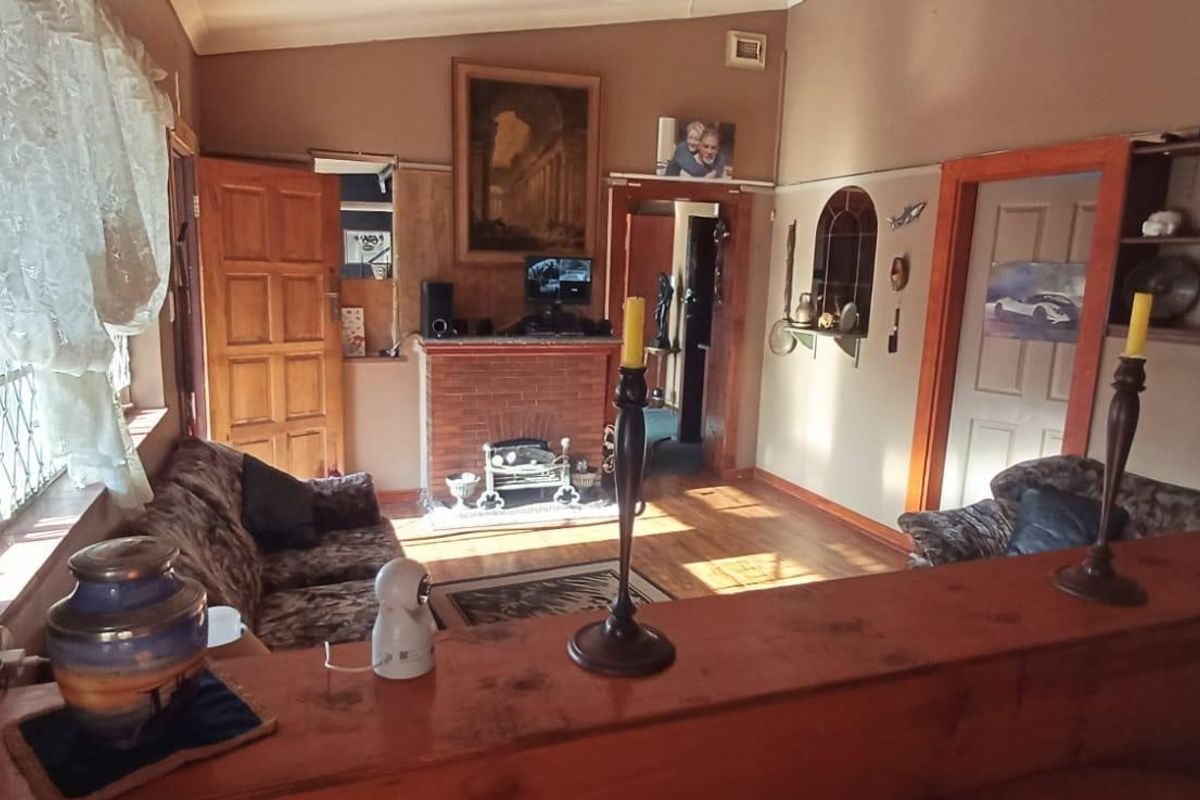 A living room featuring a brick fireplace, wooden door frames, and wooden flooring, offering a traditional layout with built-in shelving.
