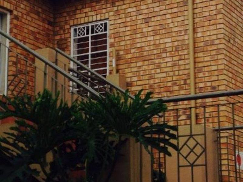 A view of the townhouse exterior featuring a face brick facade, security bars on the windows, and metal railings.