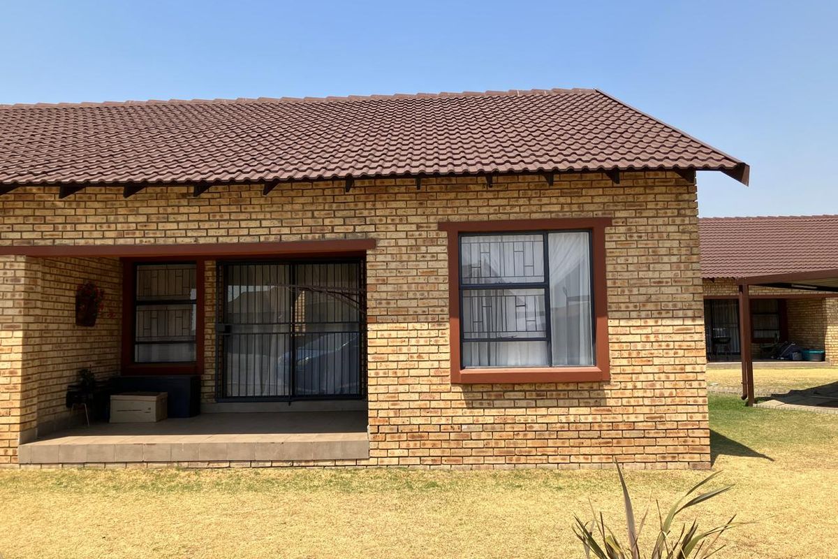 Rear view of a face brick townhouse featuring a covered patio, tiled roof, and secure window and door fittings.
