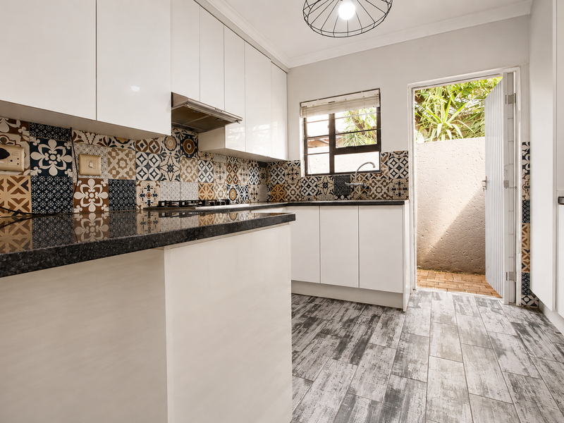 Modern kitchen featuring white cabinetry, granite countertops, patterned tiled backsplash, and direct access to an outdoor area.