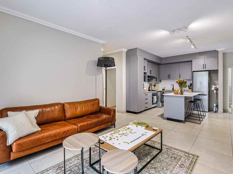 Modern open-plan living area featuring a contemporary kitchen with grey cabinetry, a central island, and sleek tiled flooring throughout.
