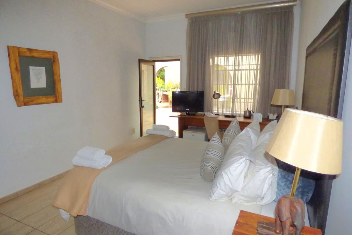 A bedroom featuring tiled flooring, a window with curtains, and a door providing direct access to an outdoor patio area.