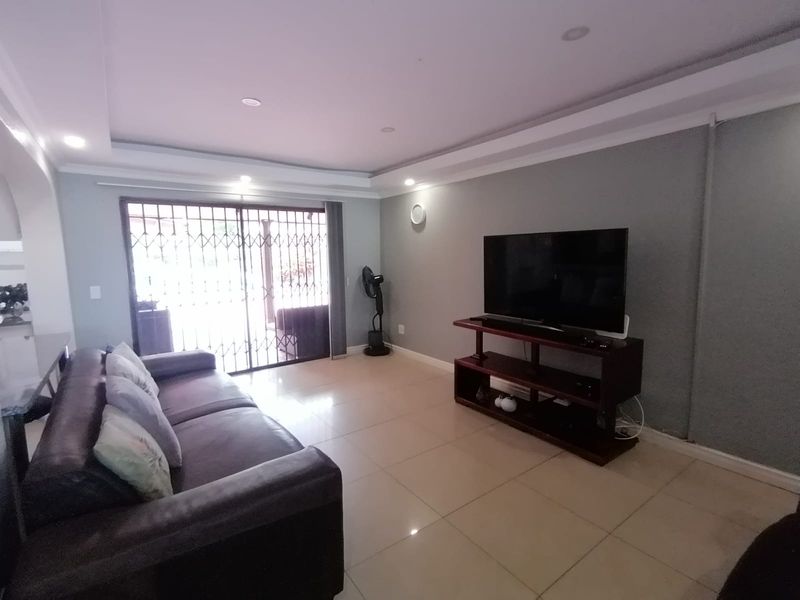 A living room featuring tiled flooring, recessed ceiling lighting, and a sliding glass door with a security gate leading to the exterior.