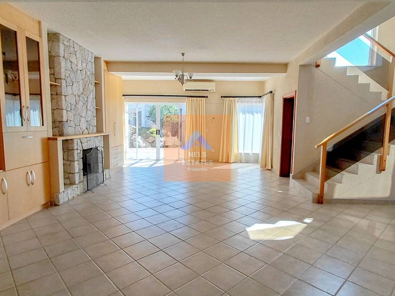 Spacious living area featuring a stone fireplace, built-in cabinetry, tiled flooring, and a modern staircase with glass balustrade, leading to a bright outdoor patio.