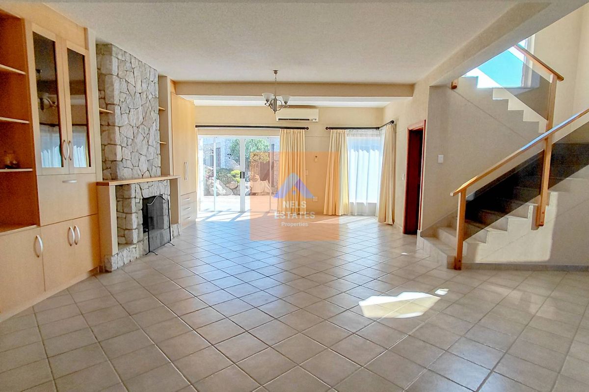 Spacious living area featuring a stone fireplace, built-in cabinetry, tiled flooring, and a modern staircase with glass balustrade, leading to a bright outdoor patio.