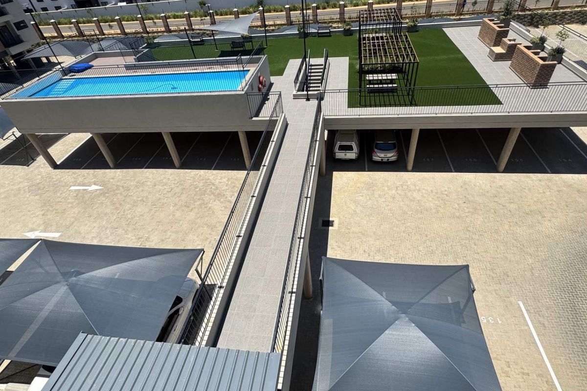 Elevated view of the apartment complex featuring a raised swimming pool, communal garden area with pergola, and covered parking bays.