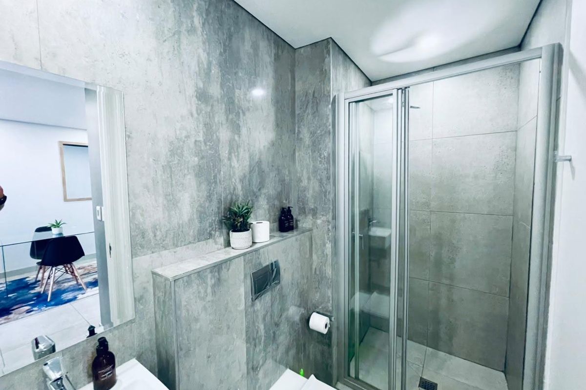 Modern bathroom featuring grey stone-look tiling, a walk-in shower with glass enclosure, and a wall-mounted toilet with integrated cistern.