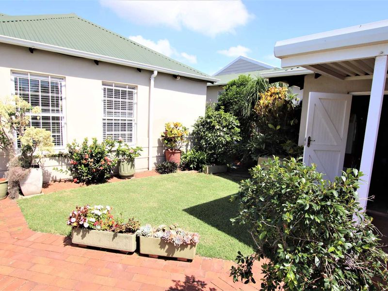 A well-maintained rear garden area featuring a brick-paved patio, manicured lawn, and established landscaping, adjacent to the main townhouse structure.
