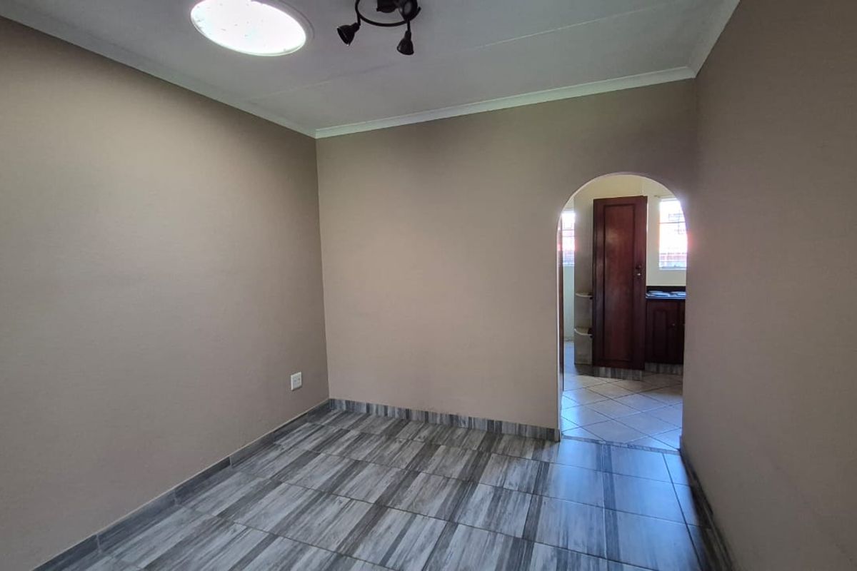 An empty living area featuring tiled flooring and an arched doorway leading to an adjacent room.