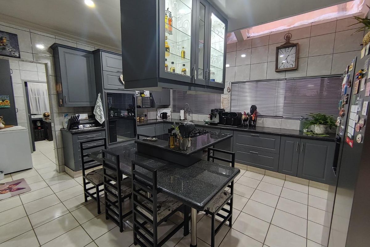 Modern kitchen featuring dark grey cabinetry, granite countertops, a central island with integrated dining space, and tiled flooring.