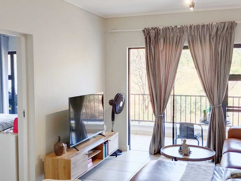 A bright living room featuring tiled floors and a sliding glass door that opens onto a private balcony with outdoor views.
