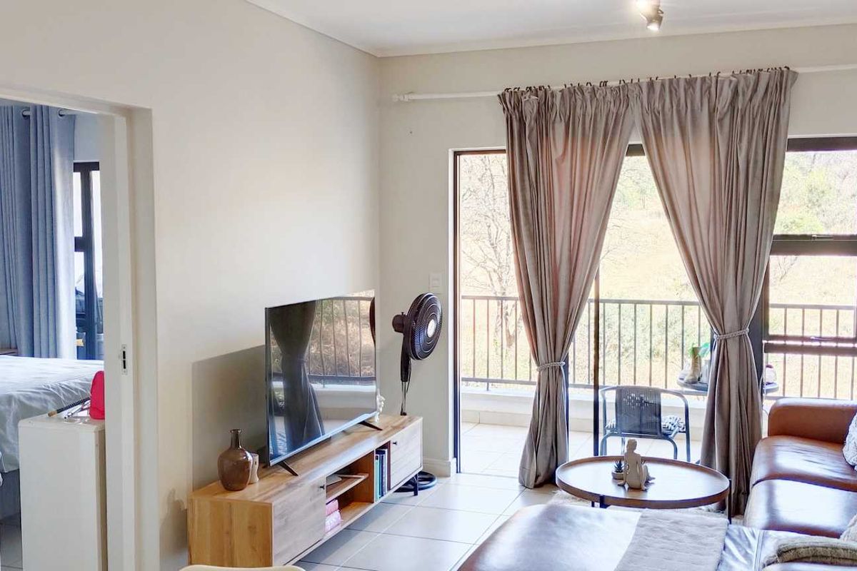 A bright living room featuring tiled floors and a sliding glass door that opens onto a private balcony with outdoor views.